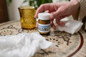 A bottle of allergy pills on a table, being reached for.