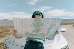 A lady reading a map while leaning against the bumper of her car.